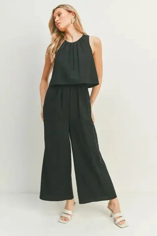 A female model showcasing a black wide-leg sleeveless jumpsuit