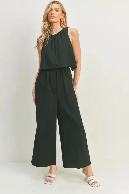 A female model showcasing a black wide-leg sleeveless jumpsuit