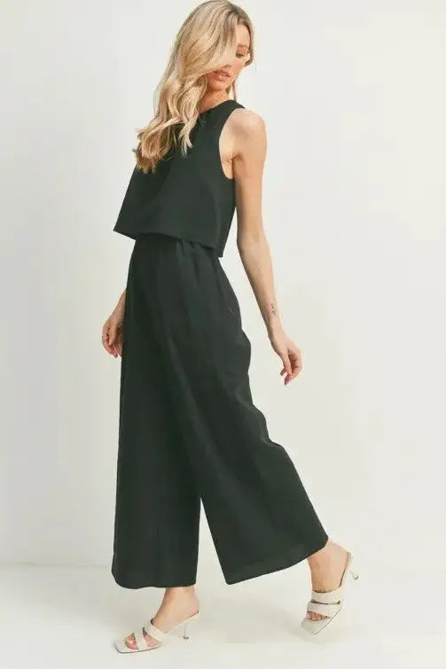 A female model showcasing a black wide-leg sleeveless jumpsuit