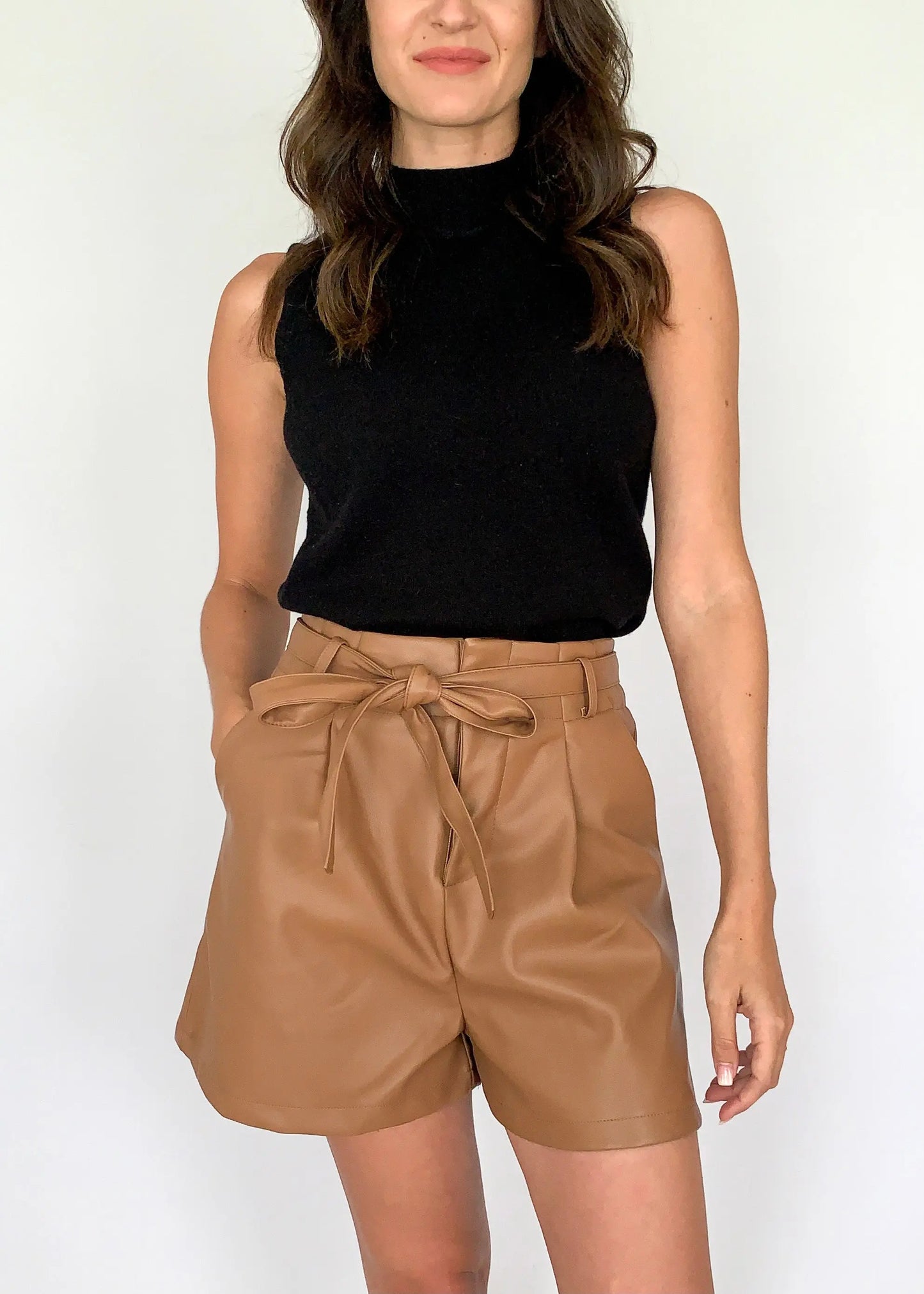 A female model dressed in a black top and large size camel leather shorts with a belt
