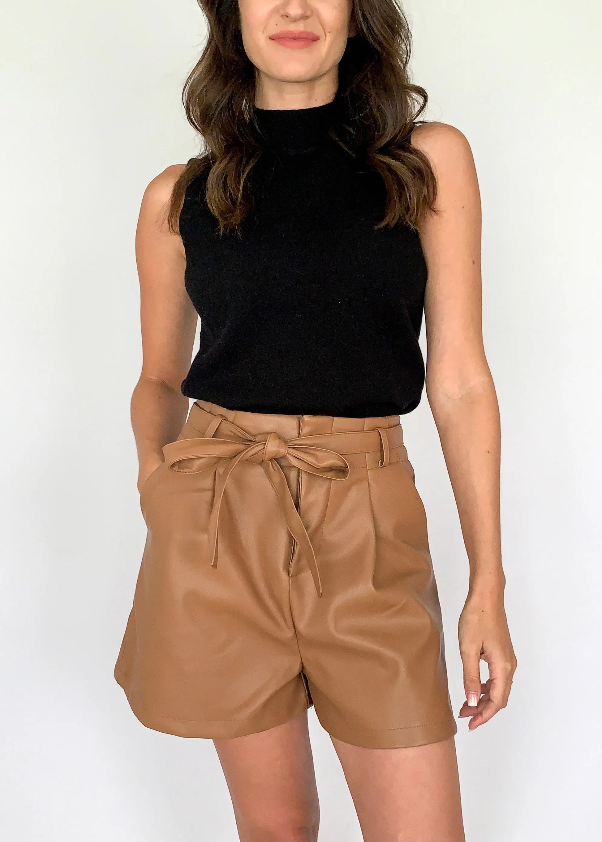 A female model dressed in a black top and large size camel leather shorts with a belt
